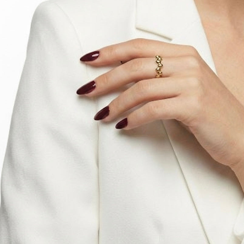 Hand wearing a gold ring with a white blazer background