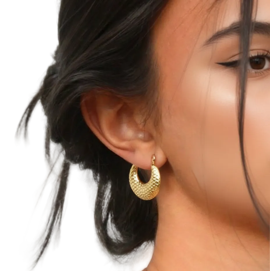 Close-up of a person wearing gold hoop earrings with a neutral background